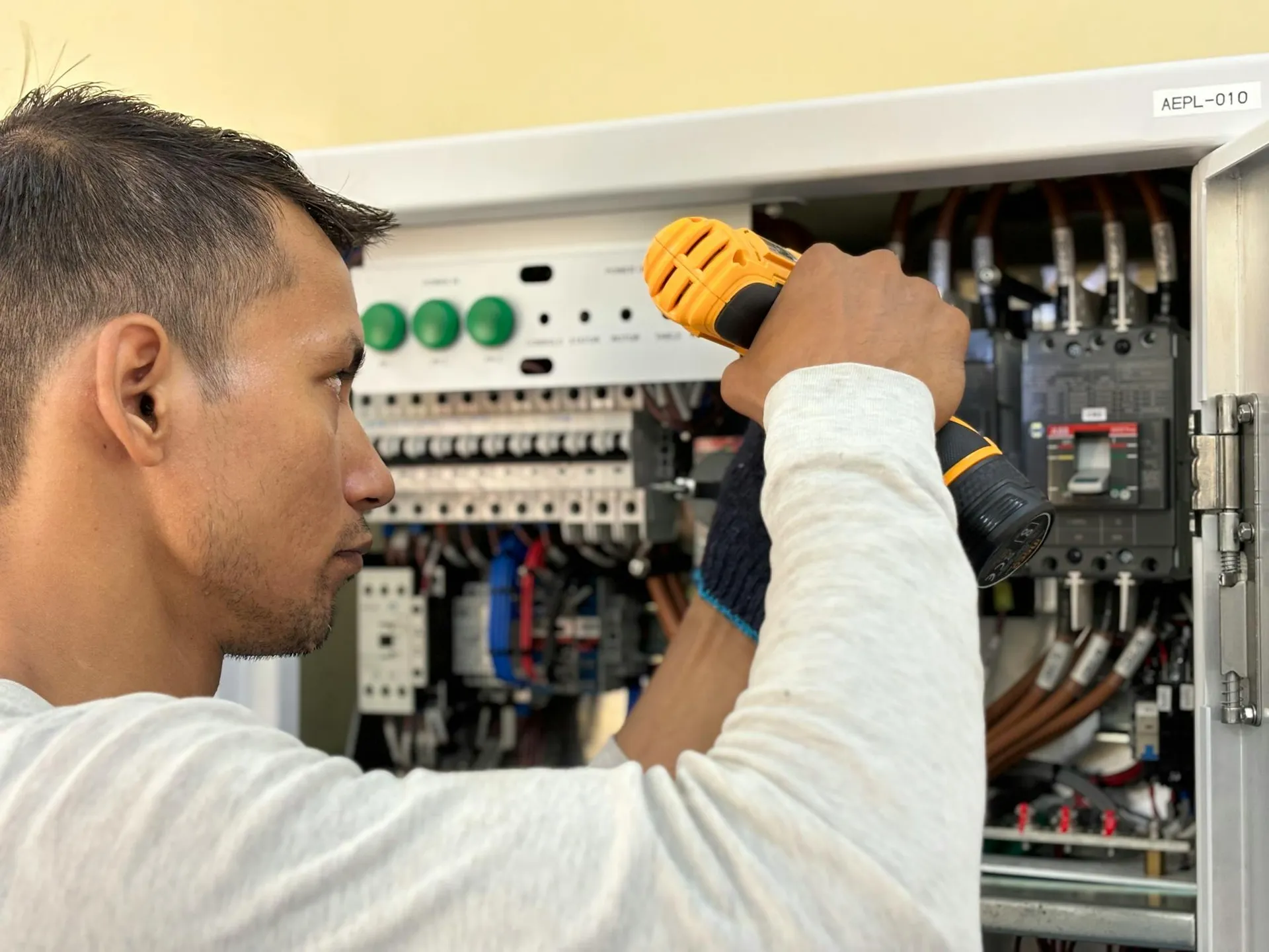 Electrician working inside an open consumer unit with a yellow drill